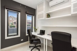 A modern office space with a desk, two black office chairs, a laptop, and a bookshelf.