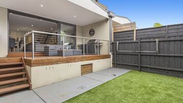 A modern house with a covered patio, a wooden staircase, and a fenced backyard.