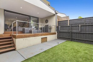 A modern house with a covered patio, a wooden staircase, and a fenced backyard.
