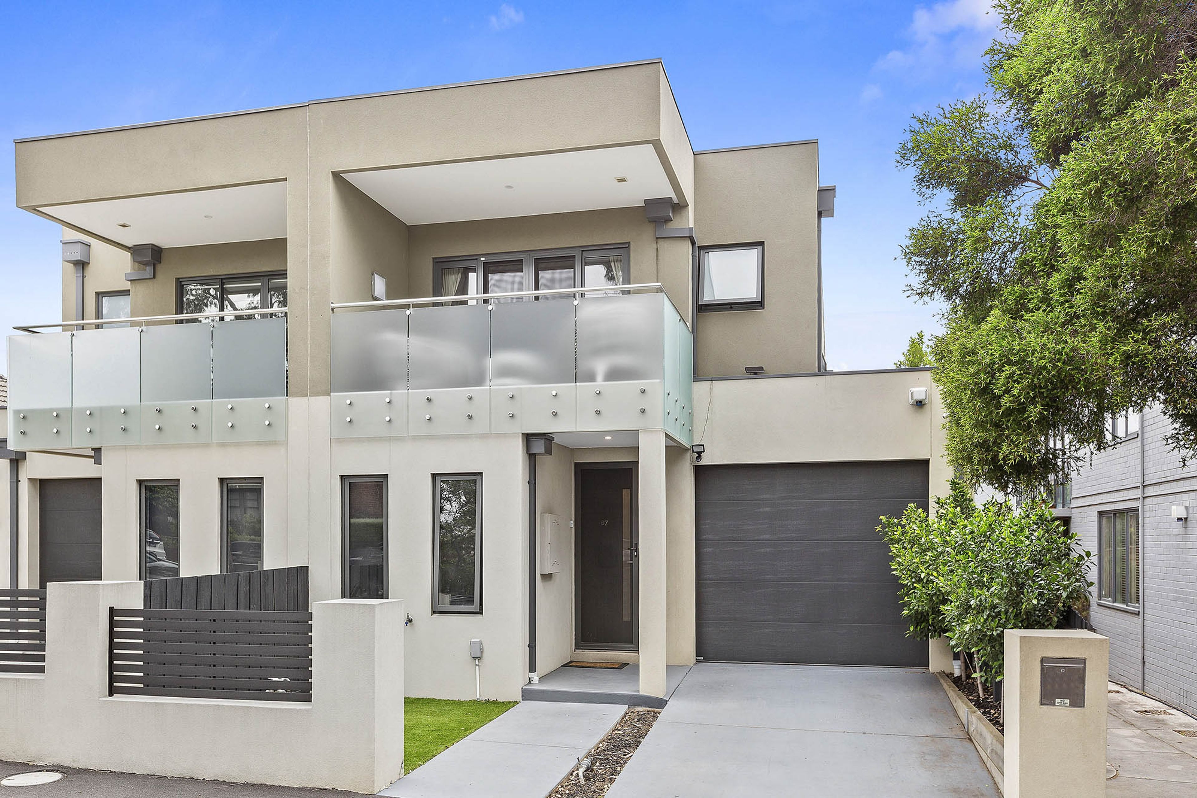 A modern two-story residential building with a balcony, a garage, and a well-maintained lawn.