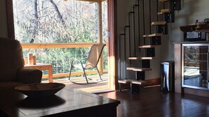 Un vaste salon doté d’un plancher en bois, d’une table à manger, d’un fauteuil à bascule et d’un escalier menant à l’étage supérieur.