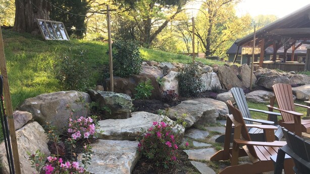 Un jardin agrémenté de gros rochers, de fauteuils Adirondack et d’une terrasse en bois.