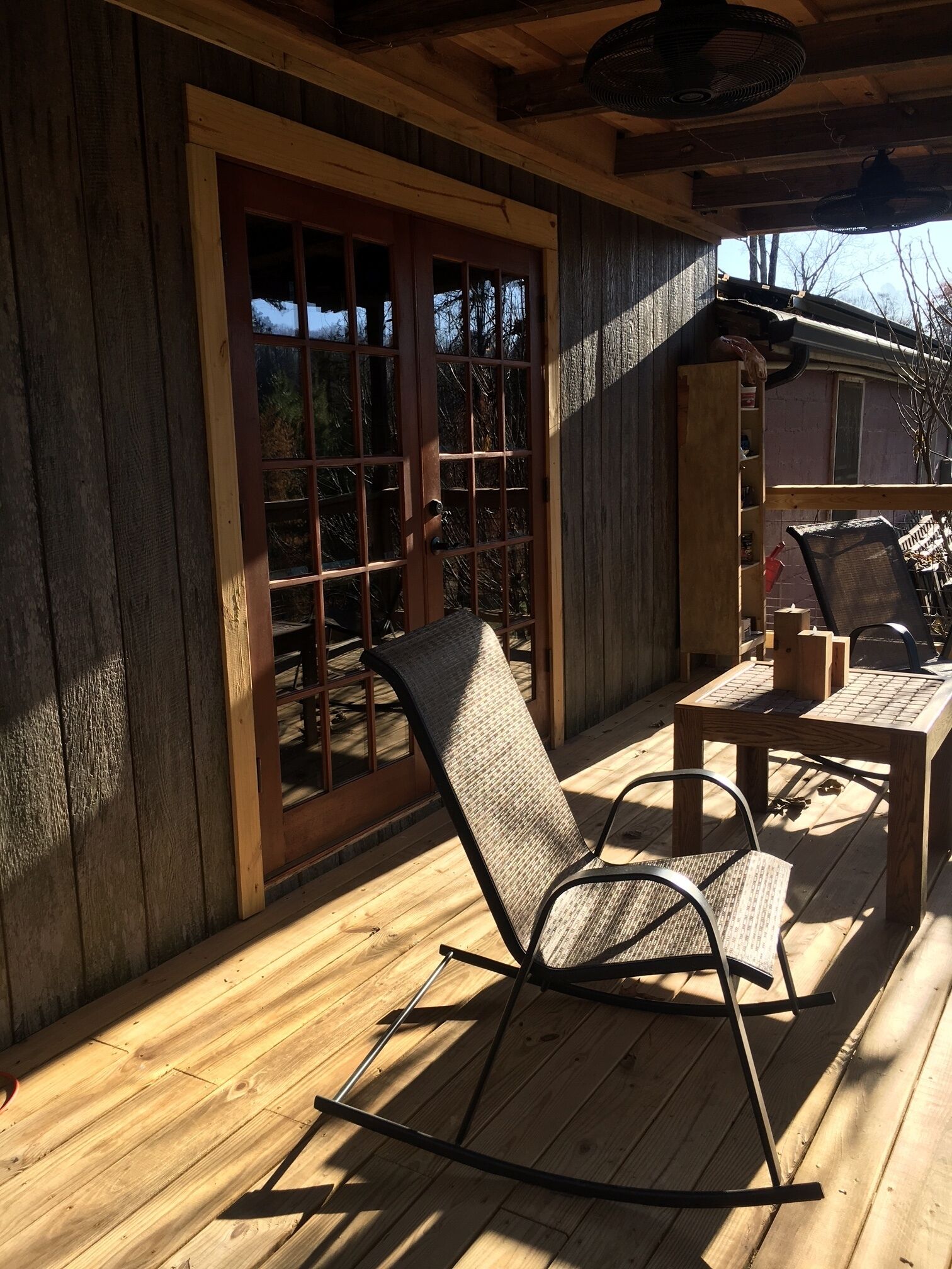 A wooden deck with a rocking chair and a table, a sliding glass door, and a fan on the ceiling.