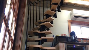 Un escalier en colimaçon en bois dans une cuisine, avec un appareil de climatisation au-dessus et un réfrigérateur en dessous.