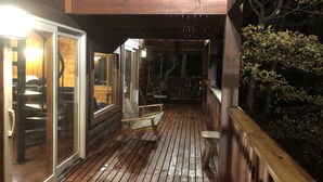 Una terraza de madera con puerta de vidrio, una silla colgante y una pequeña mesa.