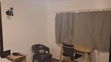 Une chambre d’hôtel comprenant un lit, un bureau, une chaise, une petite table, un téléphone et un rideau.