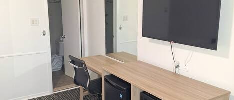 Habitación de hotel con escritorio de madera, televisión de pantalla plana, refrigerador pequeño y una silla negra.