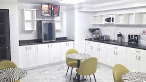 A modern kitchen with white cabinets, a black countertop, and a microwave. There are two yellow chairs around a zebra-patterned table. - Super 8 by Wyndham Montreal (Montreal)