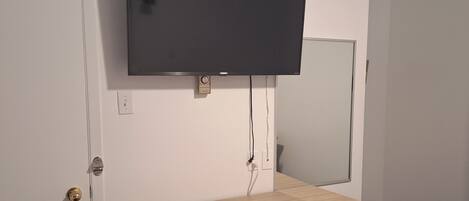 A hotel room with a flat-screen TV mounted on the wall, a wooden cabinet with a microwave, and a door with a key lock.