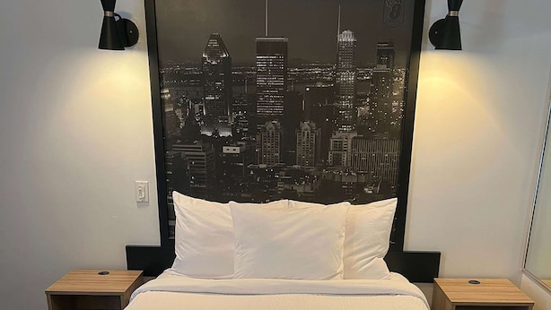 A hotel room with a bed, two bedside tables, a cityscape wall art, and a telephone on one of the tables. - Super 8 by Wyndham Montreal (Montreal)