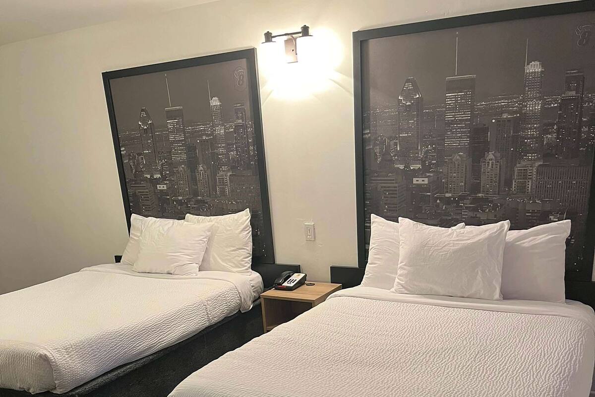 Ein Hotelzimmer mit zwei Betten, jeweils mit weißer Bettwäsche und Kopfteilen, die einen Blick auf die Stadt zeigen.