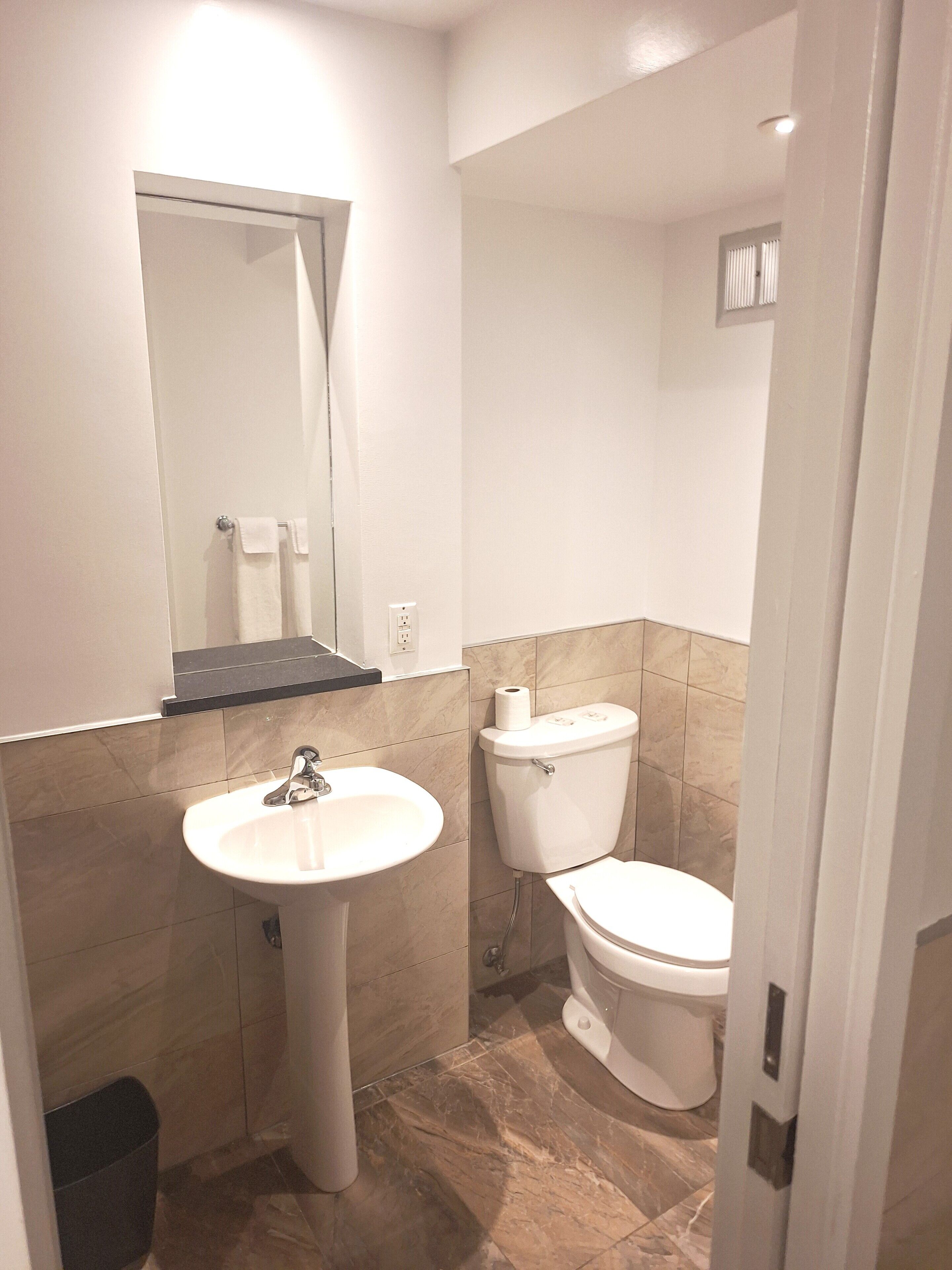 Un baño pequeño y limpio con lavamanos, inodoro y espejo.