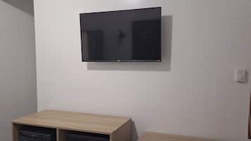 Una camera d'albergo con un letto, una scrivania con una sedia, una televisione a parete e un piccolo frigorifero.