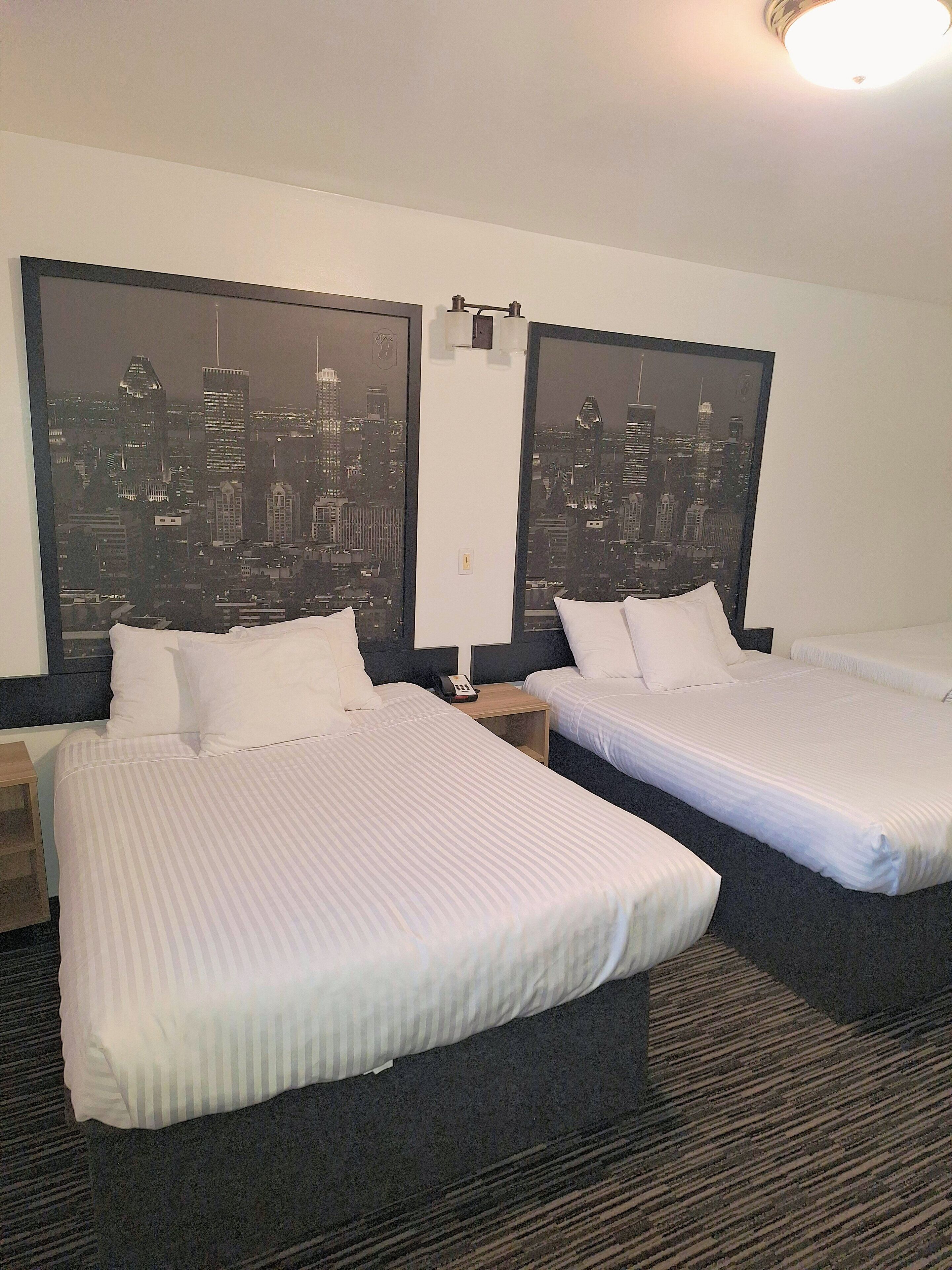 A hotel room with two beds, a nightstand, a telephone, and a cityscape view.