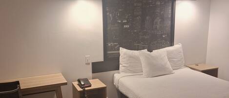 Habitación de hotel con cama, escritorio, silla, teléfono y un cartel con vista a la ciudad.