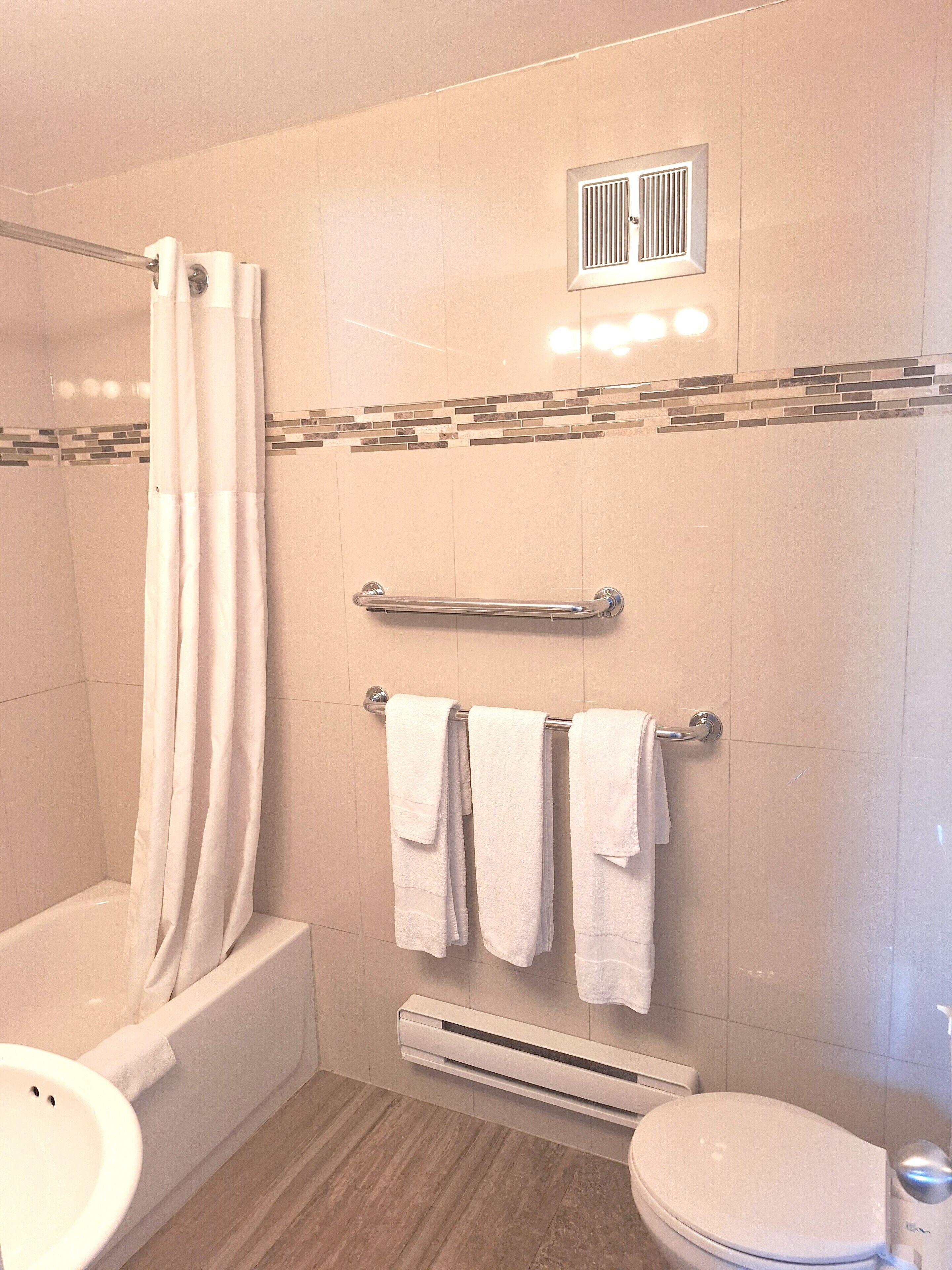 Un baño moderno con bañera, cortina de ducha, toallero y retrete.