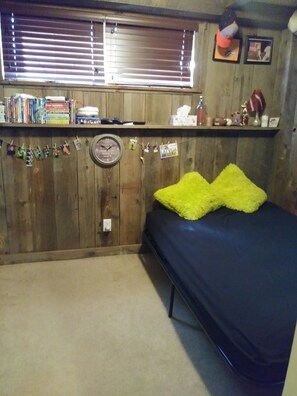 A bedroom with a bed, a wooden wall, a shelf with books and items, and a window with blinds. - 4BR/2BA Sturgis Rally 2020 Rental (Rapid City)