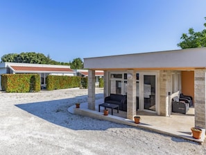 Un espace extérieur moderne, aménagé avec des sièges, une structure en pierre, une piscine et un bâtiment avec un toit rouge en arrière-plan.