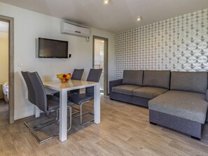 Un salon moderne avec un canapé gris, une table à manger avec des chaises et un téléviseur fixé au mur.