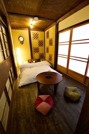 Una habitación japonesa tradicional con suelo de tatami, una cama con ropa de cama blanca, una pequeña mesa redonda y una almohada.