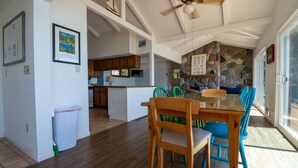 Un'ampia sala da pranzo con un tavolo e sedie in legno, una cucina sullo sfondo e un muro in pietra decorato con opere d'arte.