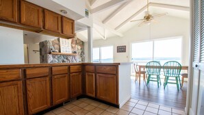 Una cucina con mobili in legno, una parete di fondo in pietra e vista sull'oceano attraverso ampie finestre.