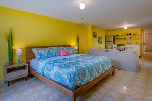 Un dormitorio con cama, mesitas de noche y una pequeña kitchenette.