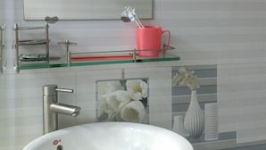 Une salle de bain avec un lavabo blanc, un miroir, un verre rouge et un vase rempli de fleurs.
