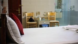 Une chambre d’hôtel avec un lit, un bureau, deux chaises et une fenêtre donnant sur l’extérieur.