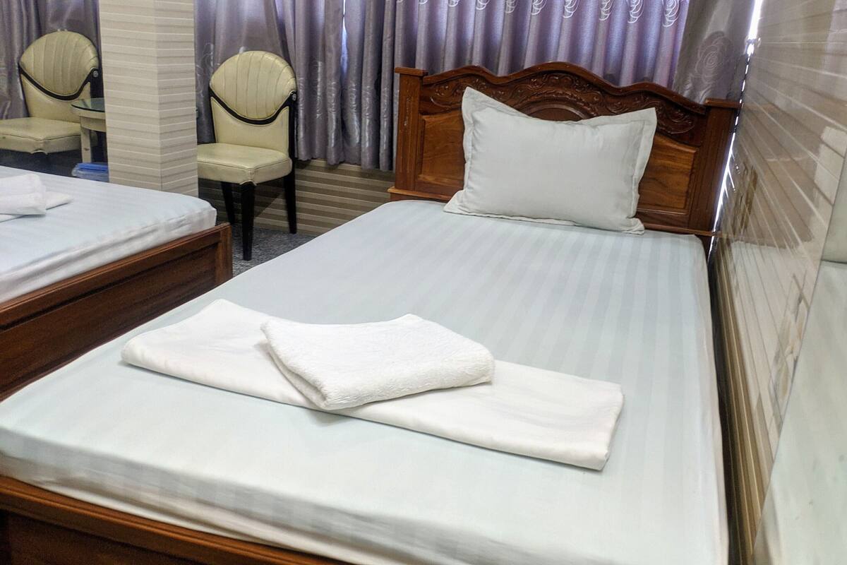 Quarto de hotel com uma cama grande, uma cama menor, uma cadeira e um espelho.