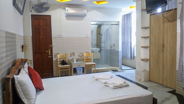 Une chambre d’hôtel comprenant un lit, un bureau avec une chaise, un espace douche et un téléviseur fixé au mur.
