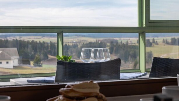 A table with a plate of pastries and a glass set on a tablecloth, with a view of a landscape through a window. - Sonnenschein (B 110) by Interhome (Dittishausen)