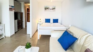A compact hotel room with a bed, a small bedside table, a white sofa, and a kitchenette area. - Sonnenschein (B 110) by Interhome (Dittishausen)