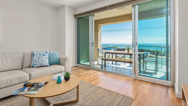 A modern living room with a sofa, coffee table, and a view of a balcony with outdoor furniture. - Sea Star - Aldinga Beach - C21 SouthCoast Holidays (Aldinga Beach)
