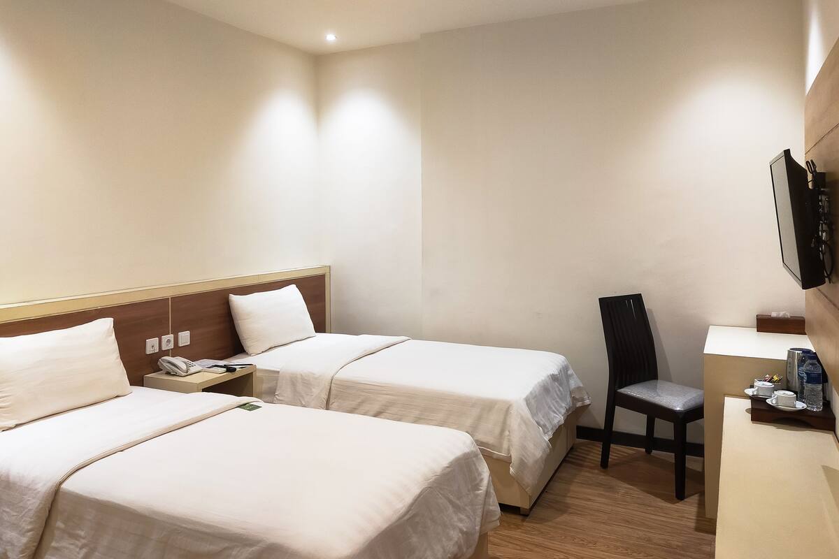Een hotelkamer met twee bedden, een bureau, een stoel en een televisie aan de muur.