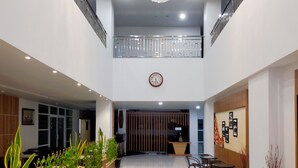 Un hall d’entrée spacieux avec un plafond haut, un lustre décoratif, une horloge et un comptoir d’accueil.