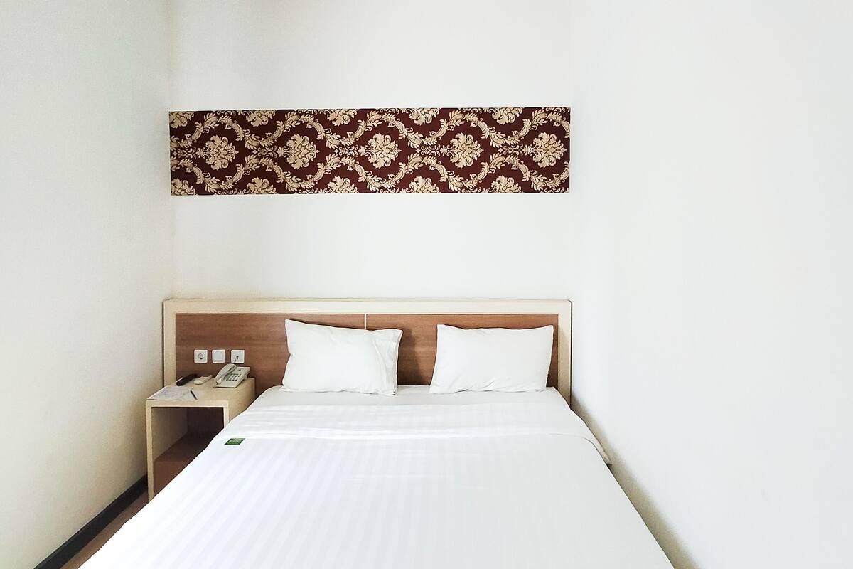 Een hotelkamer met een bed, een nachtkastje met een telefoon en een decoratief paneel aan de muur.