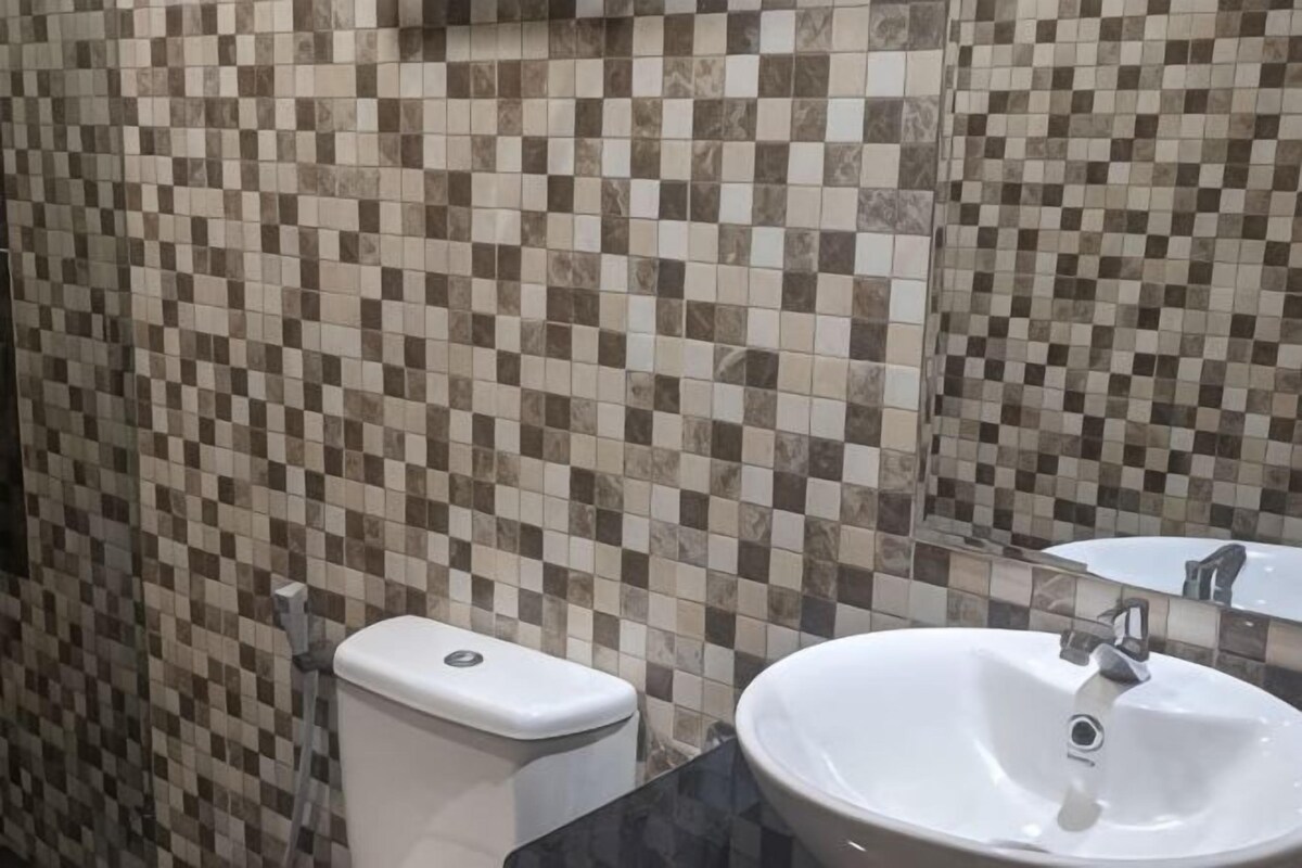 Un baño con mosaicos de baldosas a cuadros, un inodoro blanco y un lavabo con espejo.