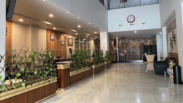 Un hall d’hôtel moderne avec un comptoir d’accueil, une horloge et une composition florale décorative.
