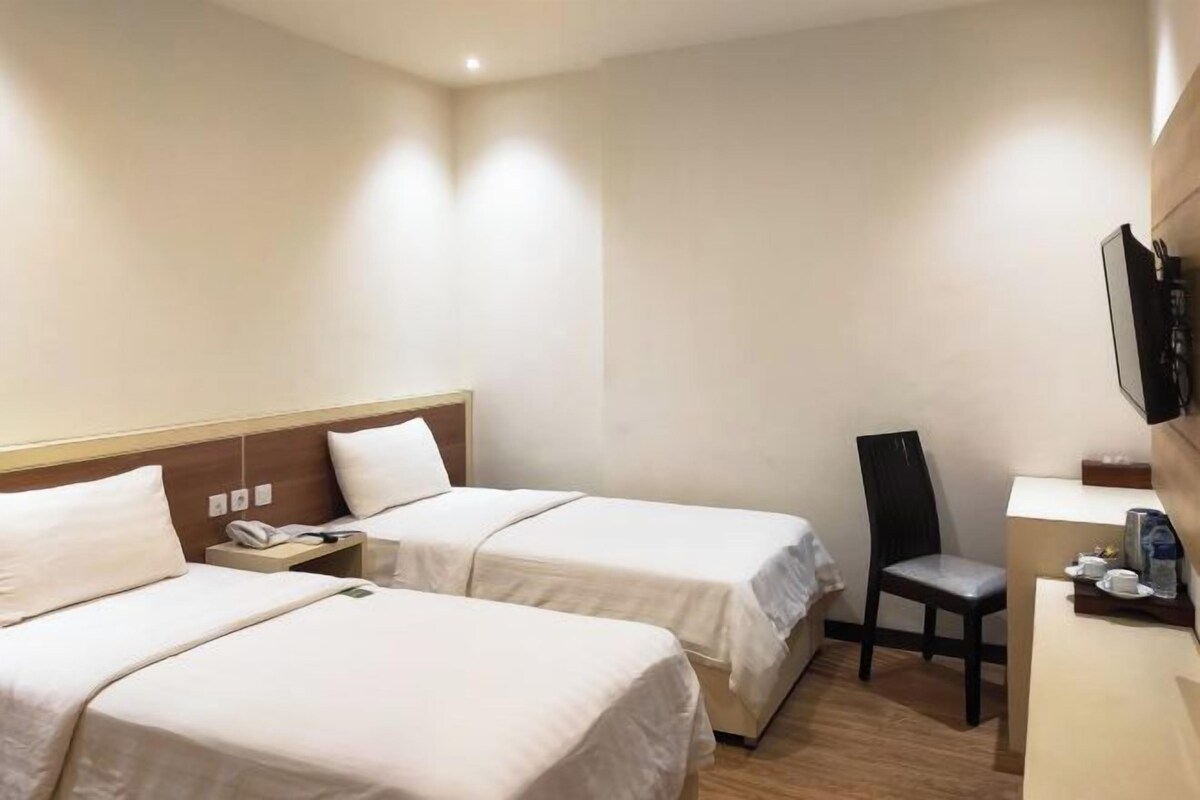 Habitación de hotel con dos camas, un escritorio, una silla y un televisor montado en la pared.