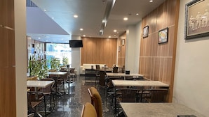 Un intérieur de restaurant moderne, avec plusieurs tables et chaises, un téléviseur à écran plat fixé au mur et un mur d’accent en bois.
