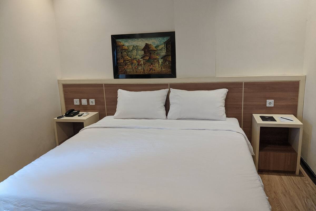 Een hotelkamer met een groot bed, twee nachtkastjes, een schilderij aan de muur en een houten hoofdbord.