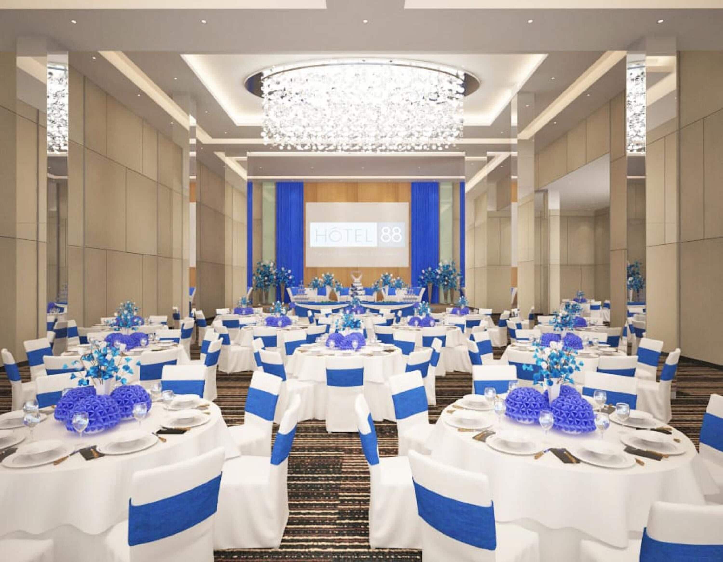 Un salón de conferencias de hotel con mesas redondas, manteles blancos, cintas azules y una pantalla grande mostrando 'HOTEL 88'.