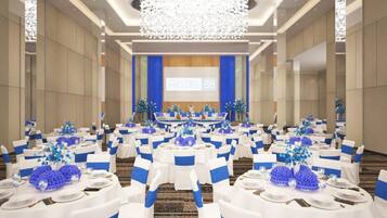 Un salón de conferencias de hotel con mesas redondas, manteles blancos, cintas azules y una pantalla grande mostrando 'HOTEL 88'.