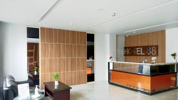 Zona de recepción de hotel con diseño moderno, que incluye un mostrador de recepción, un área de estar con sofá y una mesita, y un muro divisorio de madera.