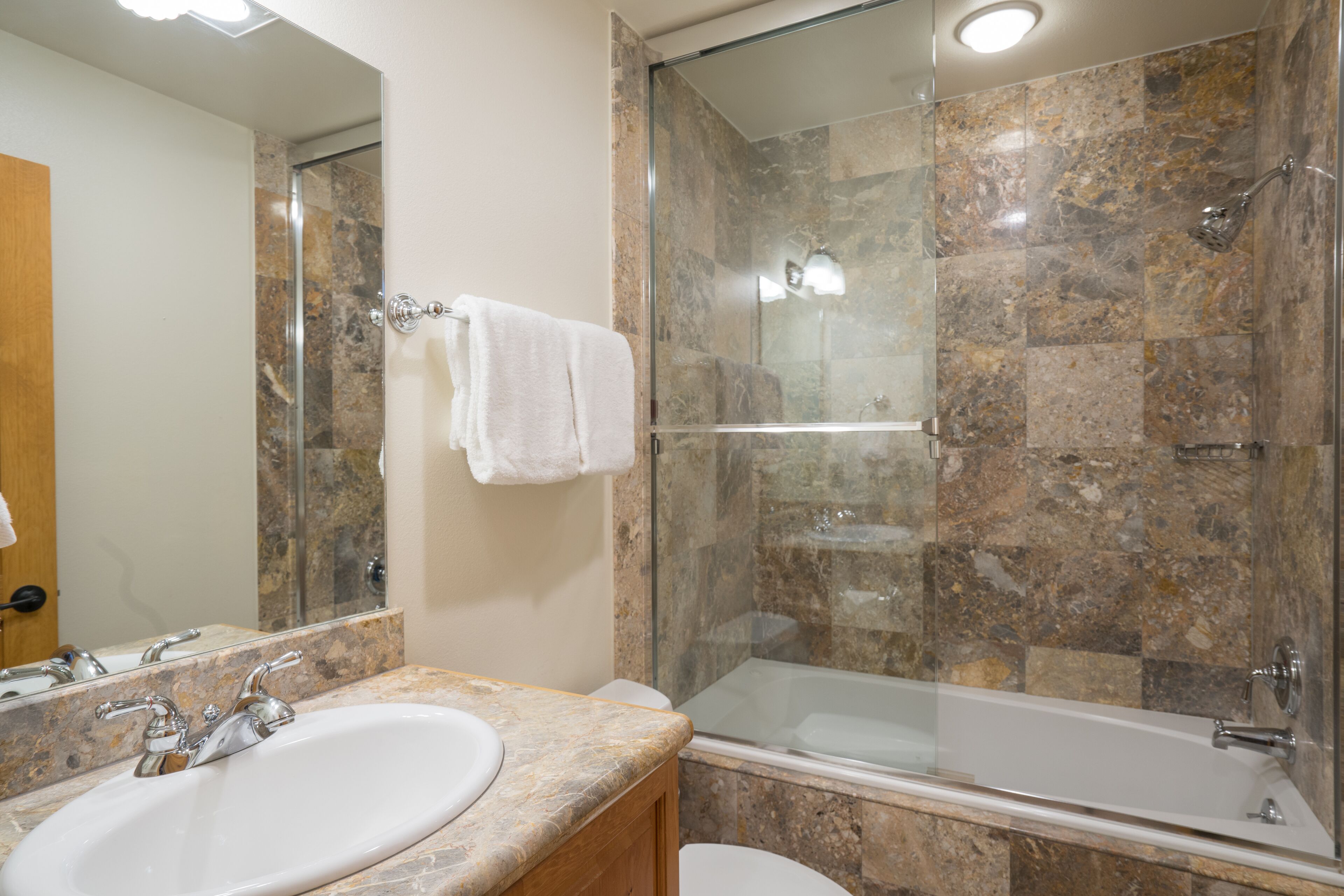 A bathroom with a marble sink, a glass-enclosed shower, and a white toilet.