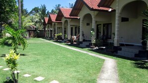 Filera d'habitacions d'hotel amb terrasses i teules vermelles, parets beix i un jardí ben cuidat amb palmeres.