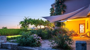 Un jardín con pérgola, mobiliario exterior e iluminación cálida en el interior de un edificio.