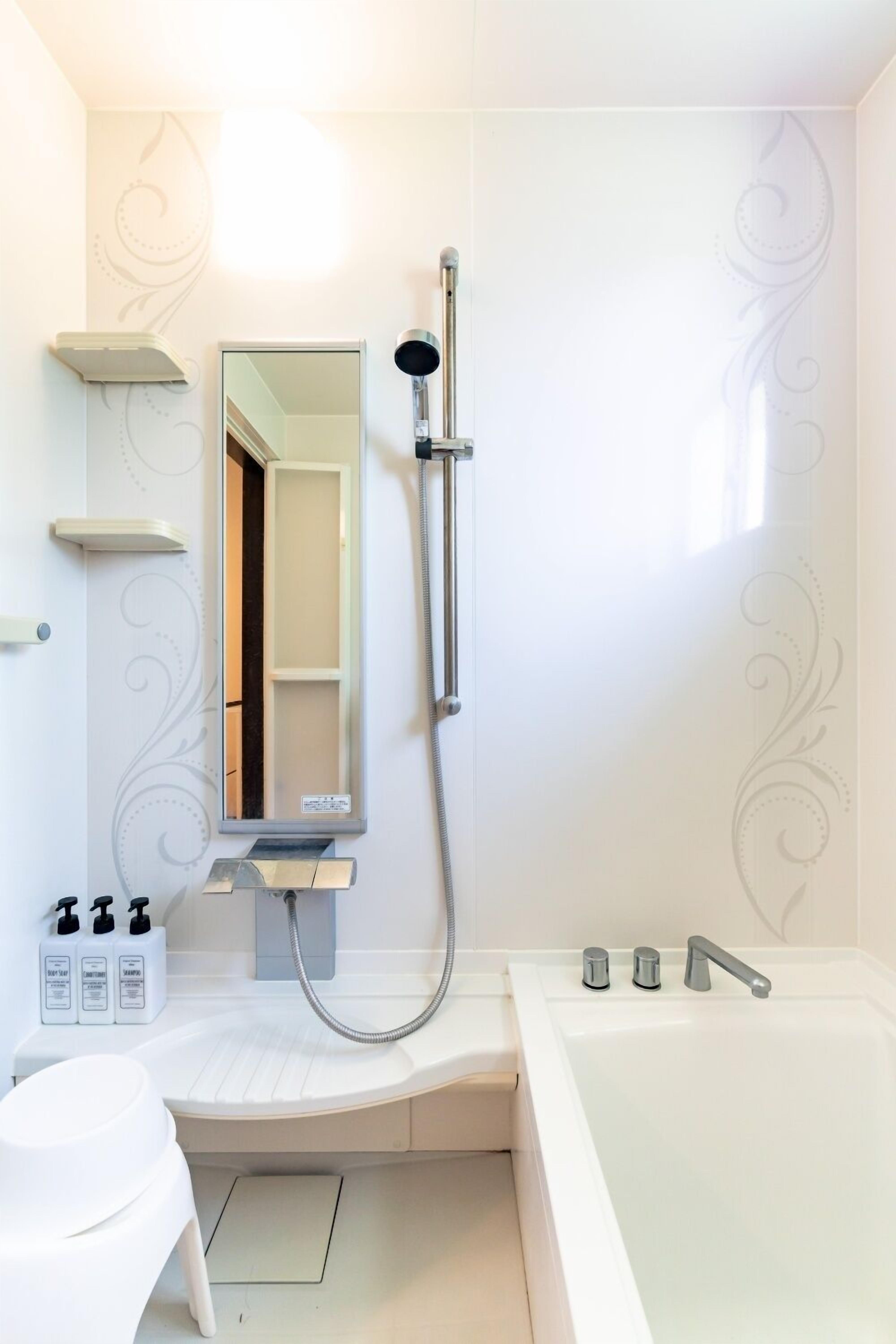 Une salle de bain moderne avec une douche, un lavabo et une baignoire. On y trouve des articles de toilette sur le comptoir et un miroir au-dessus du lavabo.
