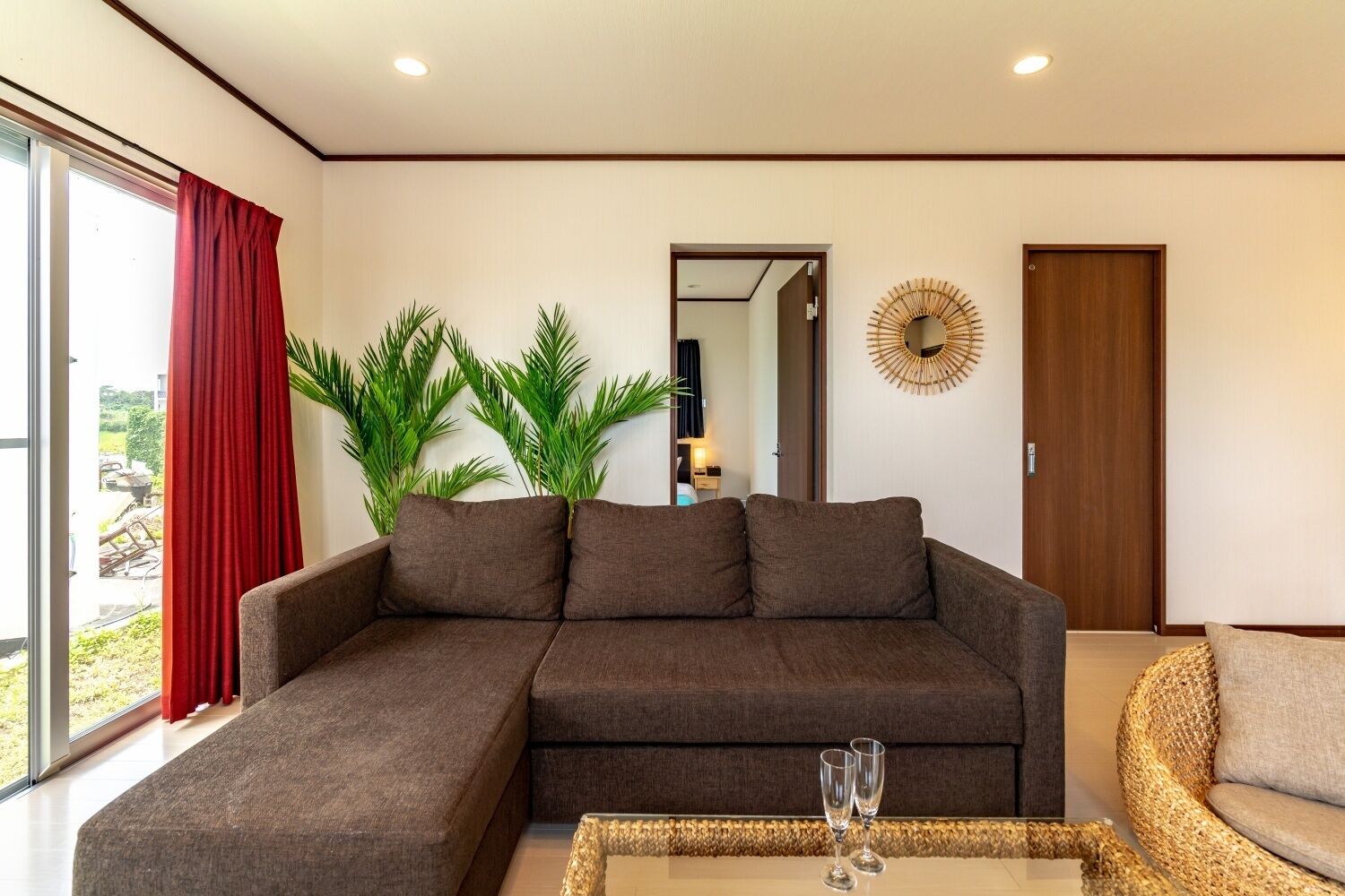 A modern living room with a sectional sofa, a wicker armchair, and a glass coffee table with two wine glasses.